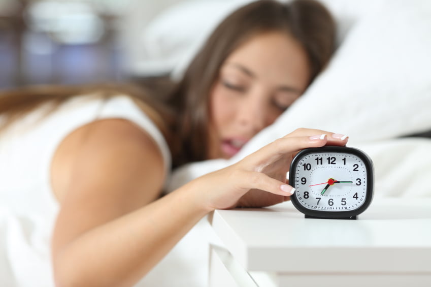 Wake up of an asleep girl stopping alarm clock on the bed in the morning